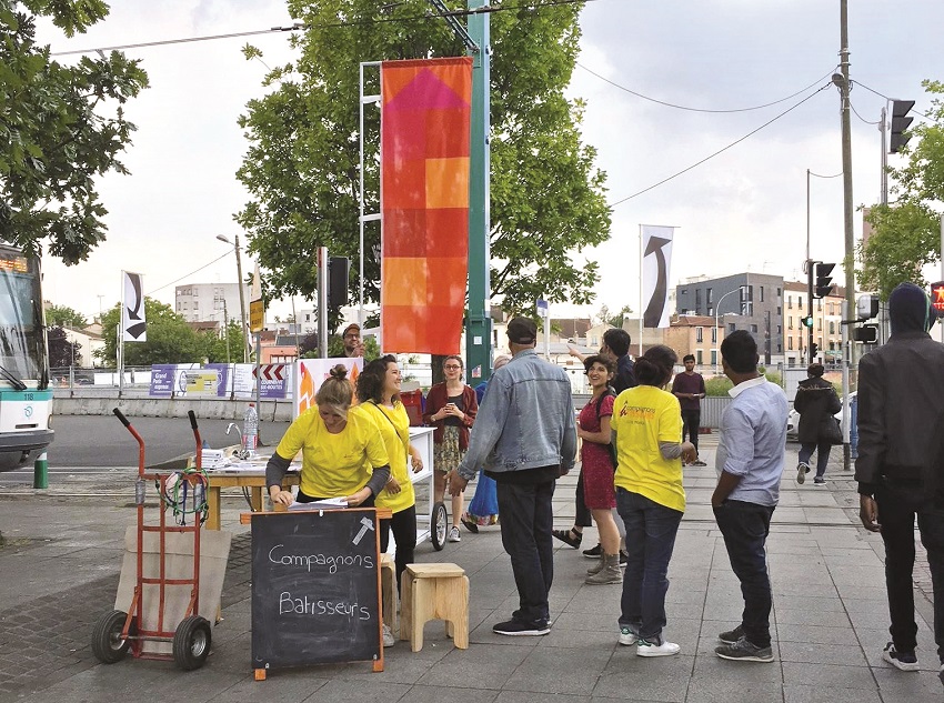 Public autour d’un stand en espace public avec un drapeau orange dans le cadre du chantier du partagé « Agrafmobile » par Malte Martin à La Courneuve en 2018