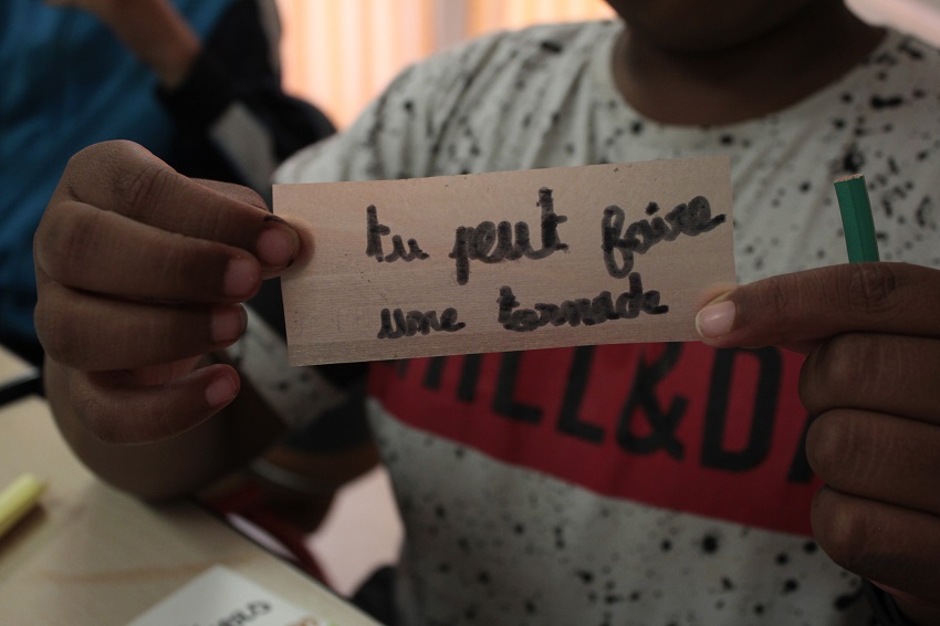 Zoom sur les mains d’un enfant tenant un panneau « tu peux faire une tornade »