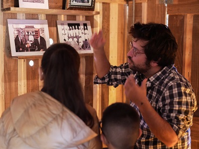 Trois personnes devant des photographies dans un des cabinets en bois dans le cadre du spectacle « Palissades » de la Compagnie Le Phun à Sevran