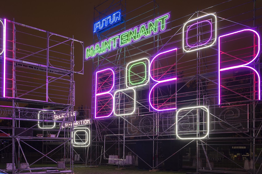 L’œuvre « Paysage vu à travers un point d’observation » composée de néons lumineux de l’artiste Tobias Rehberger, vue de près sur des néons lumineux bleux et verts qui composent les mots « maintenant » et « futur »
