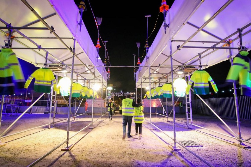 Deux séries de vestes jaunes de chantier suspendues face à face sur un chantier, avec un éclairage de nuit