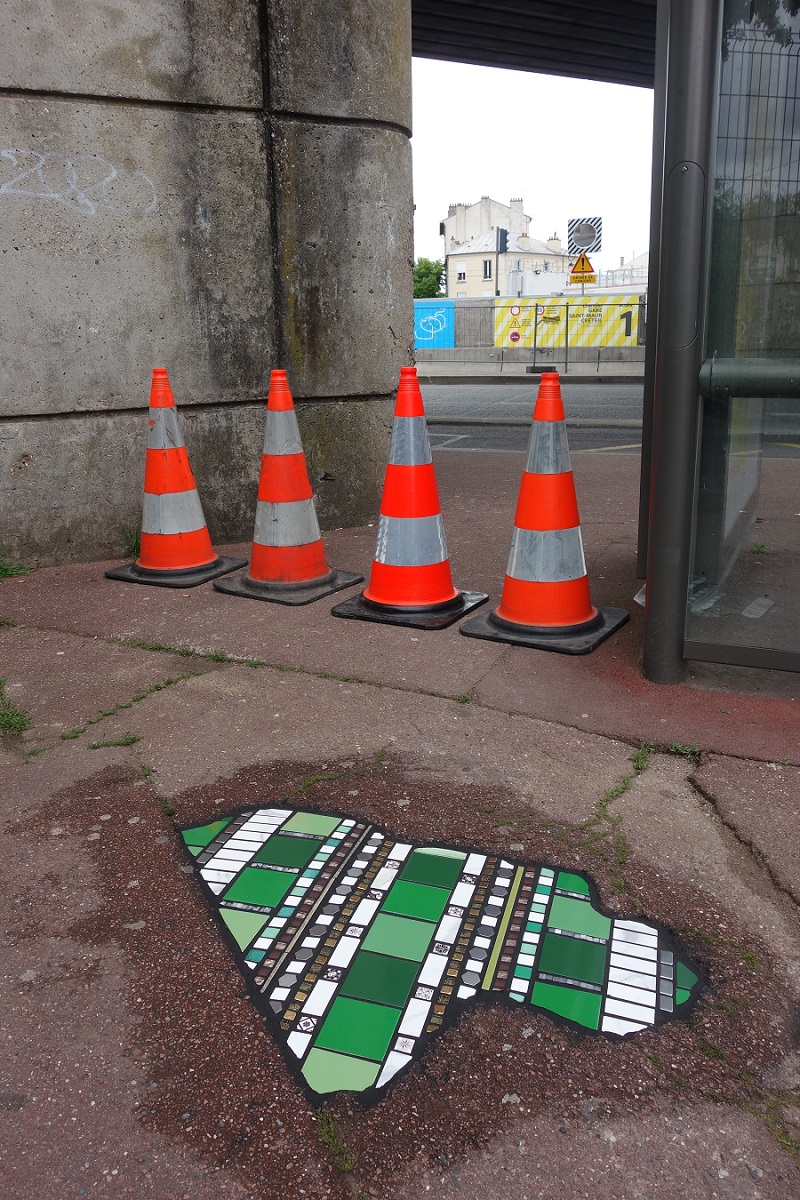 Carreaux verts et blancs en cours de séchage sur un trottoir avec 4 plots orange de signalétique en arrière-plan, dans le cadre du projet « Flacking » par Ememem à Saint-Maur