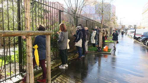 Une dizaine de personnes sont avec un stéthoscope le long de la barrière d’un parc, afin d’écouter les sons de la ville dans le cadre de la balade sonore aux abord des chantiers du Grand Paris Express d’Aubervilliers par la Compagnie Décor Sonore