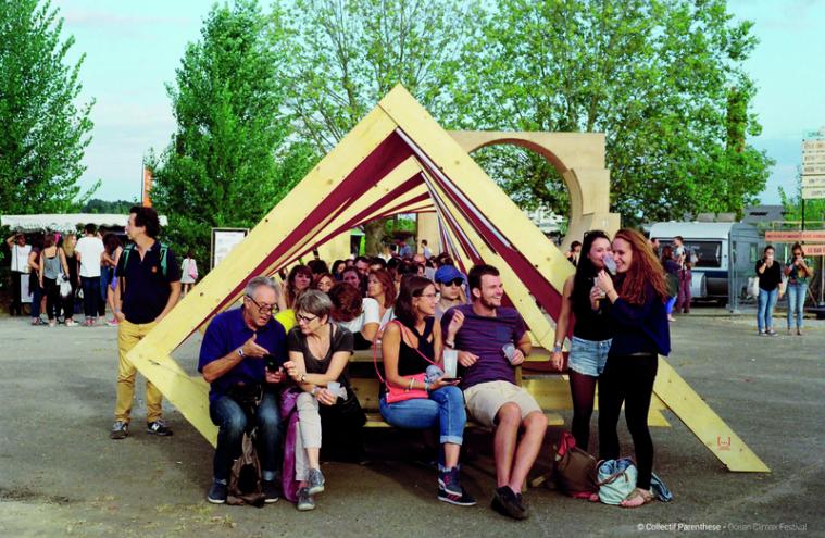 Festivaliers installés sur un mobilier urbain en bois