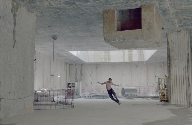 Le danseur Benjamin Bertrand torse nu en position allongée, en performance dans le chantier de l’ouvrage Salengro à Champigny