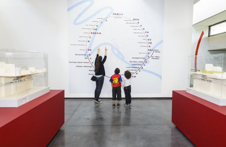 Exposition « Les Passagers du Grand Paris Express », un adulte et deux enfants observent une carte du réseau
