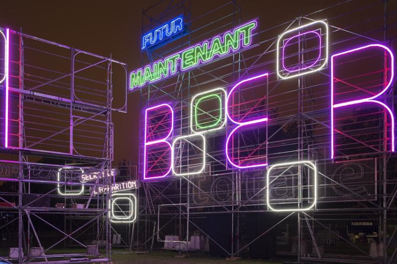 L’œuvre « Paysage vu à travers un point d’observation » composée de néons lumineux de l’artiste Tobias Rehberger, vue de près sur des néons lumineux bleux et verts qui composent les mots « maintenant » et « futur »