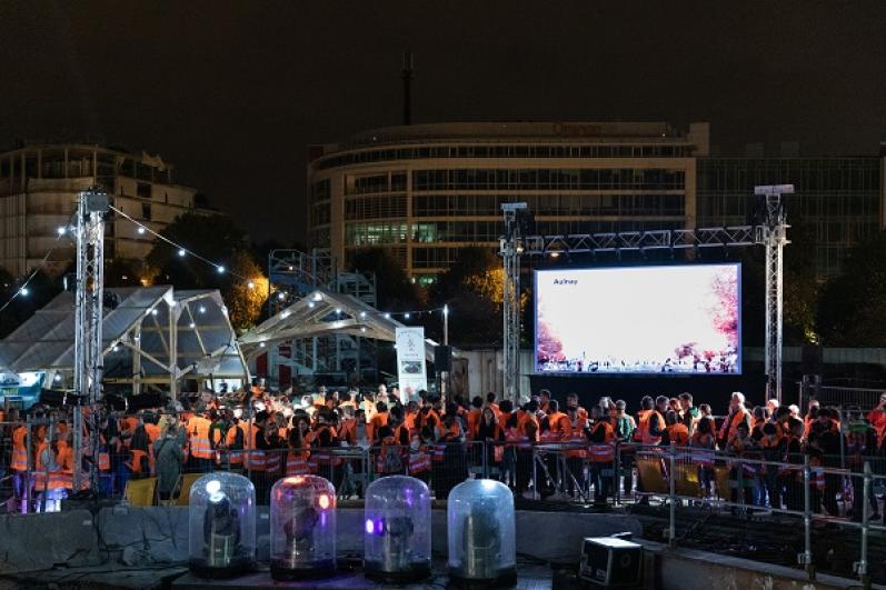 Public en gilets de chantier orange la nuit sur le chantier du puits Mandela à Saint-Denis