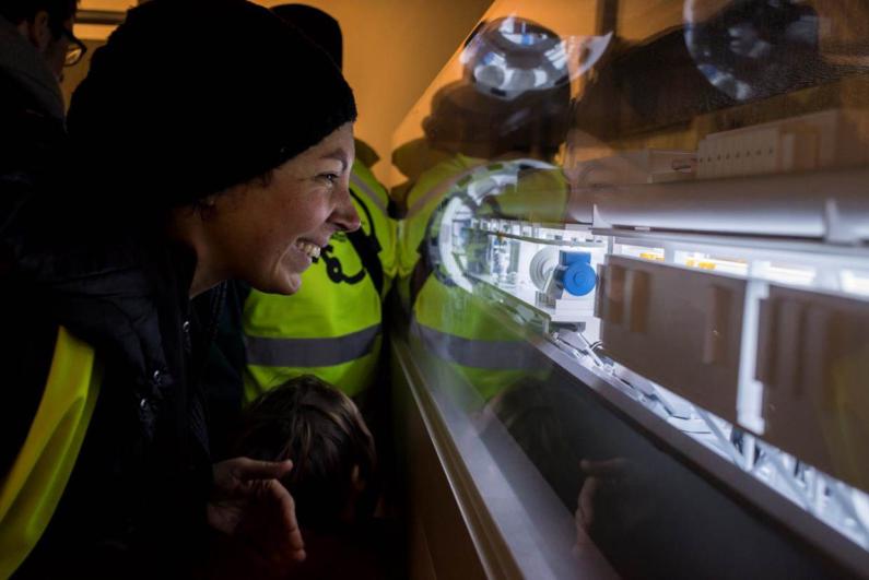 Le public en gilet jaune de chantier observe une maquette de tunnelier du Grand Paris Express sous verre