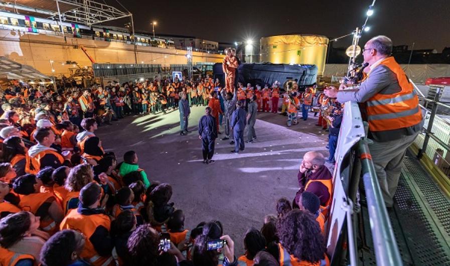 Public en gilets de chantier orange la nuit sur le chantier du puits Mandela à Saint-Denis, autour de circassiens