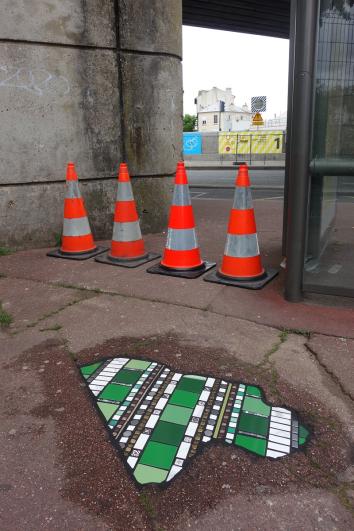 Carreaux verts et blancs en cours de séchage sur un trottoir avec 4 plots orange de signalétique en arrière-plan, dans le cadre du projet « Flacking » par Ememem à Saint-Maur
