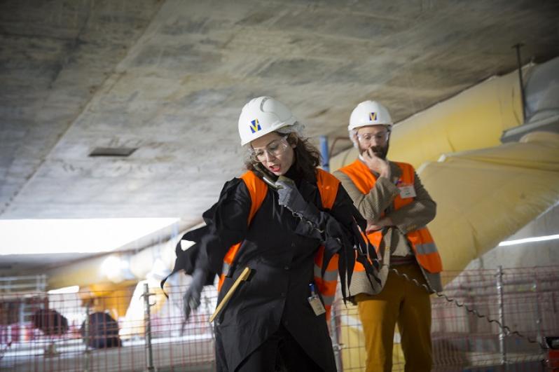 Deux comédiens en gilets de chantier orange sous le puits d’un chantier du Grand Paris Express dans le cadre du spectacle théâtralisé « Visite insolite de chantier » par la Compagnie Méliadès dans le chantier de l’entonnement Salengro à Champigny-sur-Marne en 2021