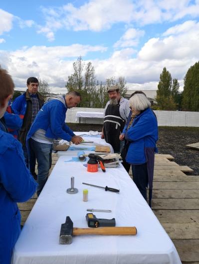Cinq personnes en bleu de travail autour d’une table blanche en train de décorer des outils, dans le cadre du projet de la Compagnie Tangible à Vitry